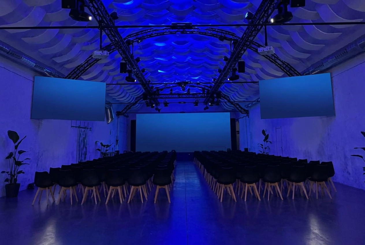 Sala Hangar de Espacio Ventas con escenario, pantallas y butacas iluminadas en azul